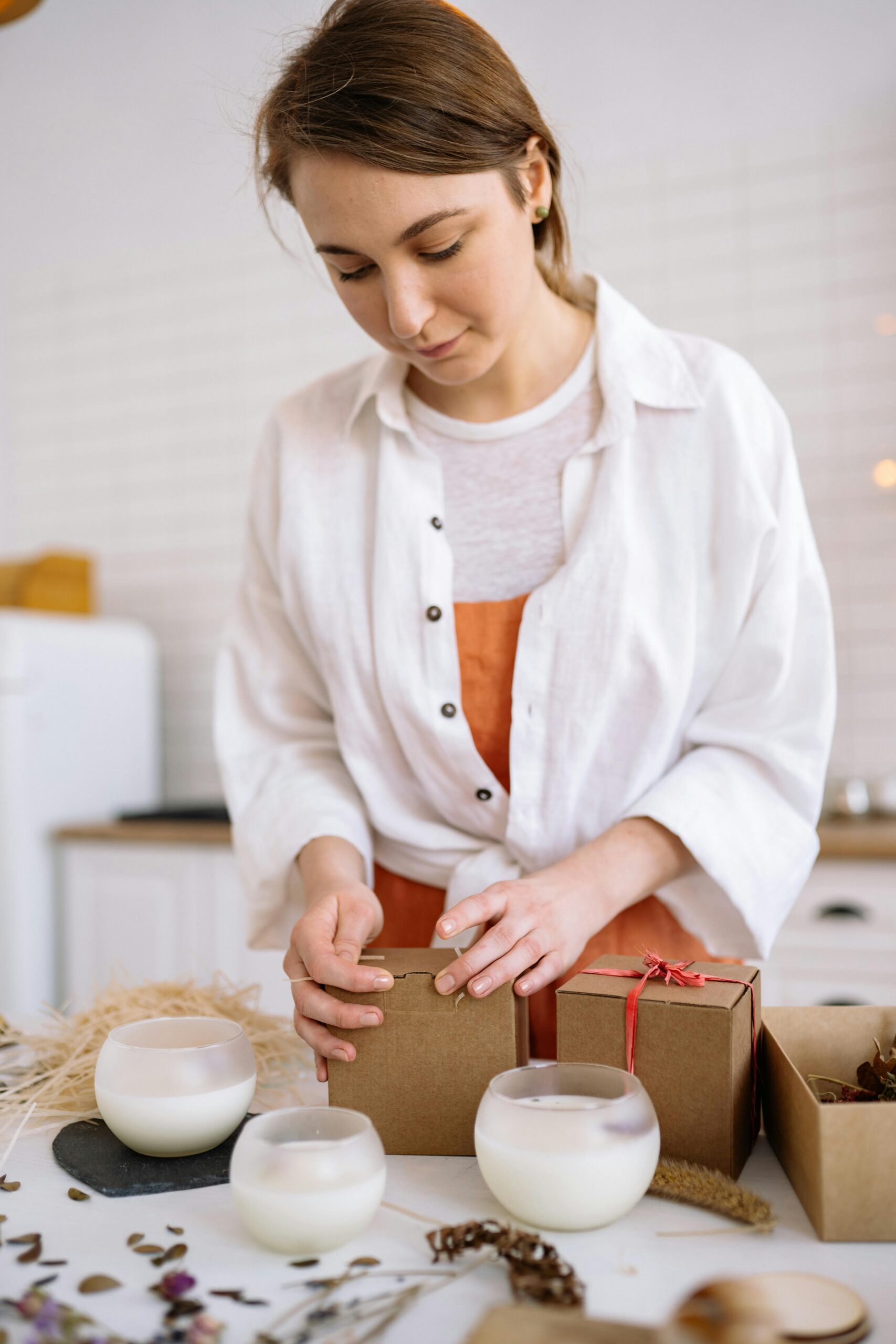 Young woman packing handmade candles into gift boxes in a cozy setting.